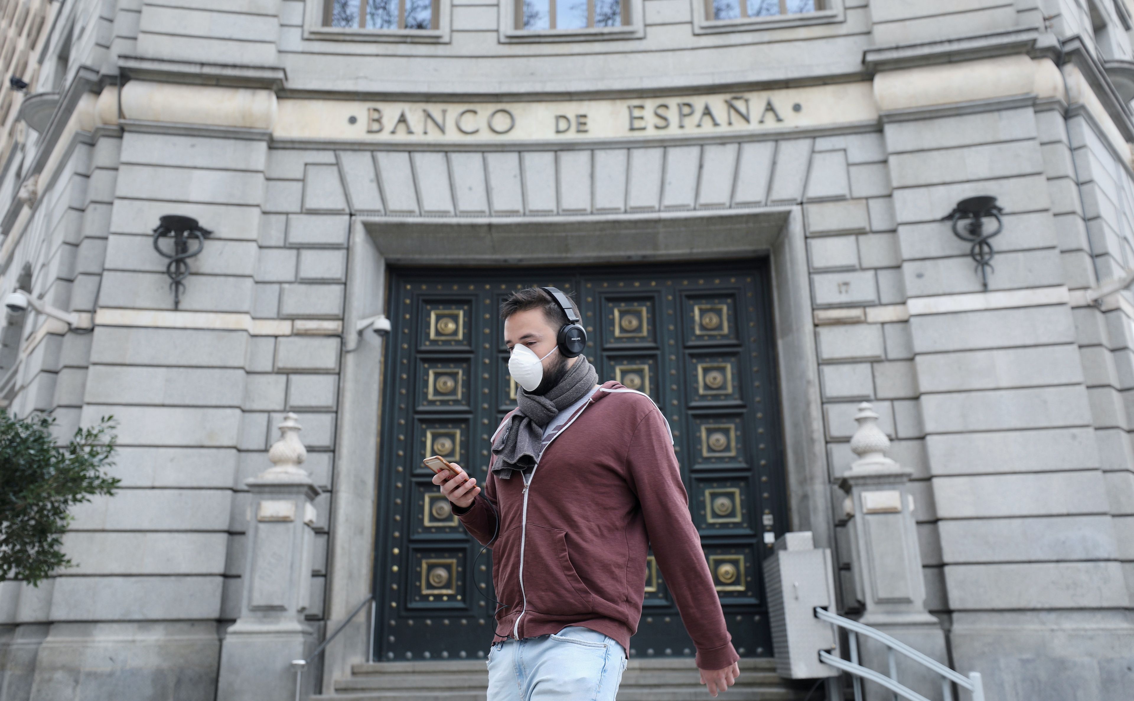 Un joven con mascarilla por el coronavirus camina delante del Banco de España